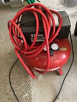 Full view of red Porter-Cable air compressor with red hose coiled on top, pressure gauge visible on tank.