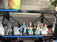 Wide shot showing assortment of angel figurines on black shelving, mixed glass and ceramic.