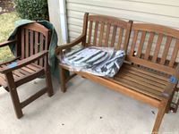 Wide view of wooden bench and armchair on patio, cushions on bench in plastic wrap, some damage visible on chair.