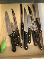Drawer view showing green-handled plastic lettuce cutter at left and assorted black-handled knives