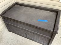 Front view of black plastic deck box showing lid and ribbed side panels.