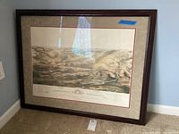 Full view of framed Gettysburg Battlefield print resting on floor against wall, showing brown wooden frame and beige matting.