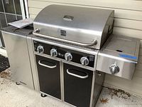 Front view of large stainless steel outdoor gas grill with control knobs and storage cabinet beneath.