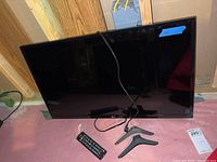 Full frontal image of the LG 32-inch TV, showing screen, LG logo, remote control, and detached feet on floor.