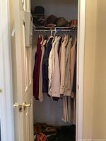 Closet showing men's winter, rain and windbreaker coats mostly size large hanging on clothing rack, with shoes and boots on the floor below.