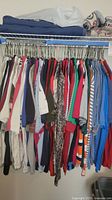 Wide view of men's shirts hanging on a rack showing variety of colors and styles including darker and lighter fabric tones predominantly long sleeve.