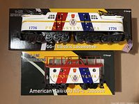 Two boxed model train cars displayed on floor, locomotive on top box and caboose on bottom box