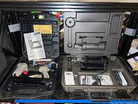 Photo showing both the Porter-Cable Brad Nailer in beige with case and papers, and the Rotozip Spiral Saw kit in a dark case on a lower shelf.