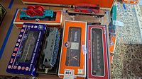 Top view of six model train cars in original packaging including Lionel and American Railroad Legends Series.