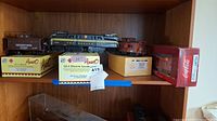 Four model trains on shelving with boxes, including Pennsylvania caboose, GG-1 electric loco, Lehigh Valley loco, and Coca-Cola car