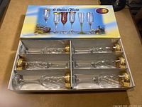 Box containing six Calici flute glasses with gold trim arranged side by side.