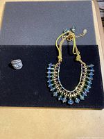 Photo of Ali Khan necklace with iridescent beads and Himalayan Jewelry gold-tone ring with clear stones on black background.