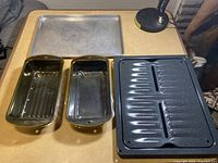 Baking set shown on a table including two loaf pans, a metal cookie sheet, and the broil pan with grid top.