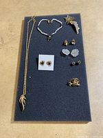 Full display of costume jewelry items including necklace, bracelet, multiple pairs of earrings, and brooches on a black foam board.