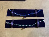 Two costume jewelry bracelets displayed on navy blue velvet holders. One bracelet has blue oval stones, the other has green oval stones. Both have clear rhinestones and silver-tone metal settings.