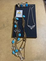 Photo showing the three jewelry pieces: a long gold-tone necklace with turquoise and clear beads, a silver-tone floral rhinestone necklace, and a gold-tone bracelet with turquoise and clear stones.