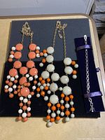 Image showing two multi-colored bead necklace with gold-tone chains plus silver-tone link bracelet on dark blue display.