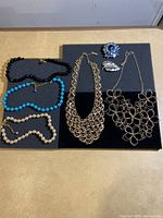 Overview of all five necklaces and two brooches displayed on black mats and a wooden surface.