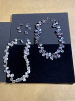 Full view of two necklaces on black felt, with a pair of drop earrings on the upper left.