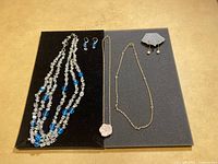 Set of costume jewelry displayed on black foam, including bead necklace, matching earrings, gold-tone chain necklaces, and pearl earrings.