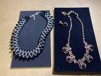 Photo showing one black and silver bead woven necklace and another gold-tone necklace with dark teardrop stones alongside matching earrings.