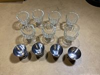 Eight egg holders, four clear glass with a fluted design and four metal with a rounded cup and base.