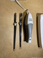 Photo shows electric handheld cutter with two blades placed beside it on a table.