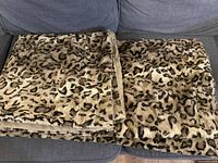 Leopard print faux fur blanket folded on a couch, showcasing the faux fur texture and pattern.