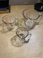 Overview of three glass measuring cups in varying sizes on a wooden surface.
