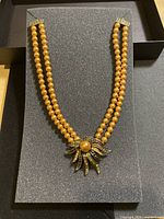 Full view of the double strand necklace showing gold tone beads and sunburst pendant.