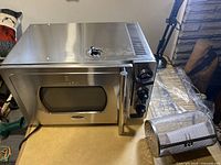 Front and side view of stainless steel Kitchentek pressure oven with control knobs and viewing window, showing sealed valve on top.