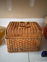 Large rectangular woven wicker basket with hinged lid and two handles placed on top, visible from the front showing texture and size.