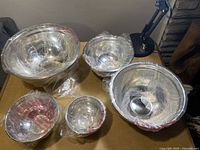 Top view of all 5 stainless steel mixing bowls wrapped in protective plastic, showing different sizes.