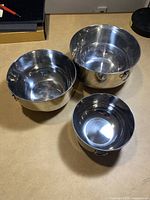 Three stainless steel mixing bowls in various sizes placed on a flat surface, showing overall condition and handles.