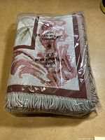 New woven throw blanket with dusty rose and green floral pattern and fringe edges in original plastic packaging