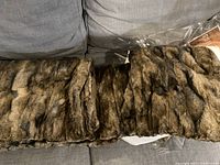 Photo showing entire faux fur blanket laid out on gray couch for scale and texture visibility.