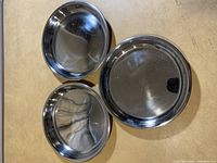 Top view of three stainless steel shallow pans arranged on a surface showing their round shape and reflective finish.
