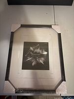 Full front view of unopened black picture frame with cardboard corner protectors and protective plastic wrapping.