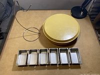 Small metal six loaf pans, metal banana holder, and plastic Tupperware pie carrier with lid displayed on a table.