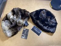 Photo showing two women's winter hats made of faux fur in light and dark color patterns with tags