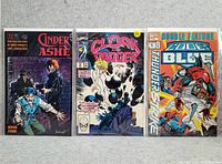 Photo shows three vintage comic books set side by side on a gray surface. Covers are visible, displaying titles Cinderella Ashes Book Four, Cloak and Dagger, and Double Feature: Code Blue and Thunder Strike.