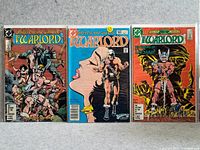 Photo showing all three Warlord comic covers laying flat on a gray surface, arranged side by side, showing cover art and issue details.