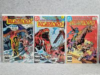 Photo of three vintage Warlord comics laid out side by side showing the front covers. The first comic depicts a Viking ship on rough seas with warriors. The second shows a giant sea reptile attacking a ship. The third shows a battle with warriors wielding spears and weapons on a boat.