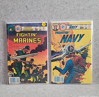 Two vintage military-themed comics Fightin' Marines and Fightin' Navy in plastic protective sleeves on a grey surface.