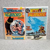 Photo shows two Warlord comics side by side on gray background, with clear plastic covers. Covers show full color artwork with titles and issue numbers visible.