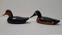 Pair of two wooden duck sculptures displaying side views on white background.