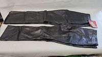 Two pairs of black leather pants laid flat, one with original tags visible
