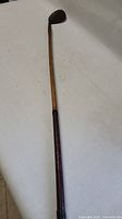 Full length view of the antique niblick wooden golf club showing wooden shaft and dark grip.