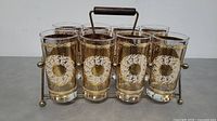 Front view of 8 clear glass tumblers with gold decorative patterns in metal carrying rack.