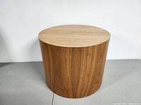 Front view of cylindrical teak side table on gray surface